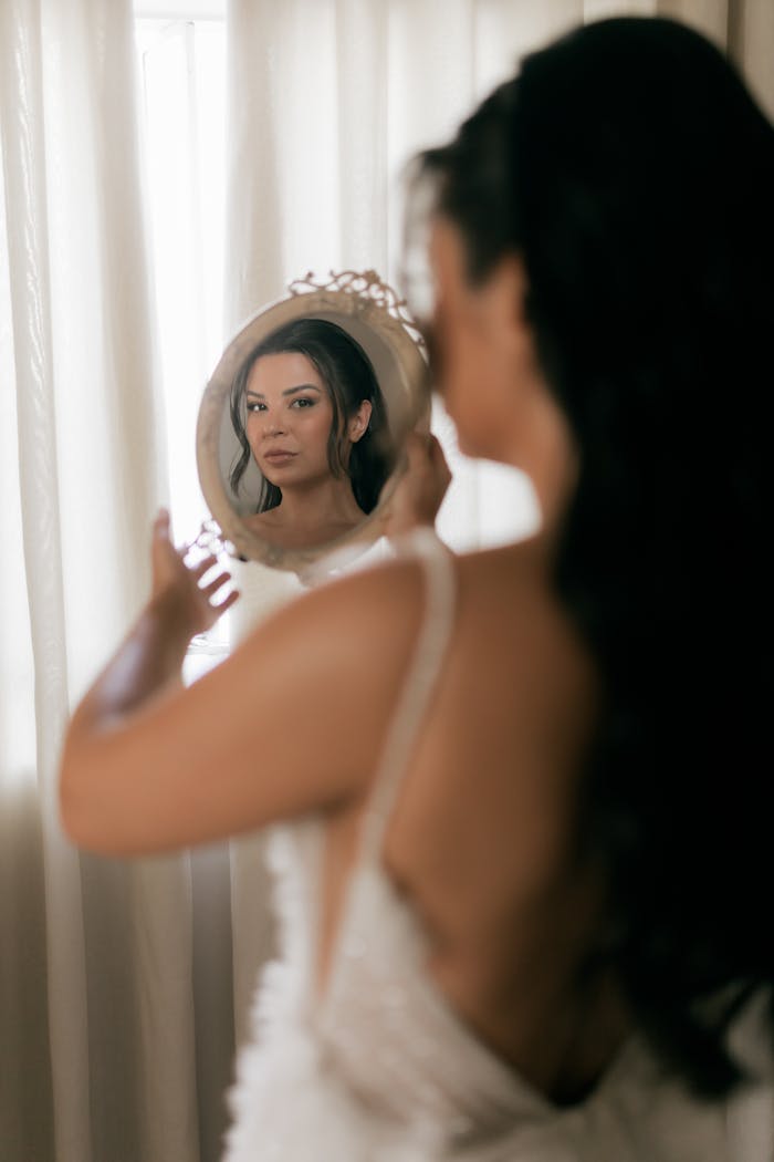 Bride preparing for wedding, gazing in antique mirror, elegant moment captured indoors.