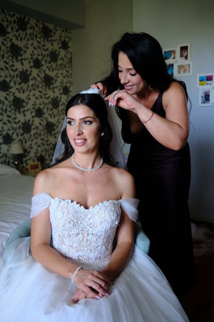 A bride prepares for her wedding day as a woman adjusts her veil in a warmly lit room.