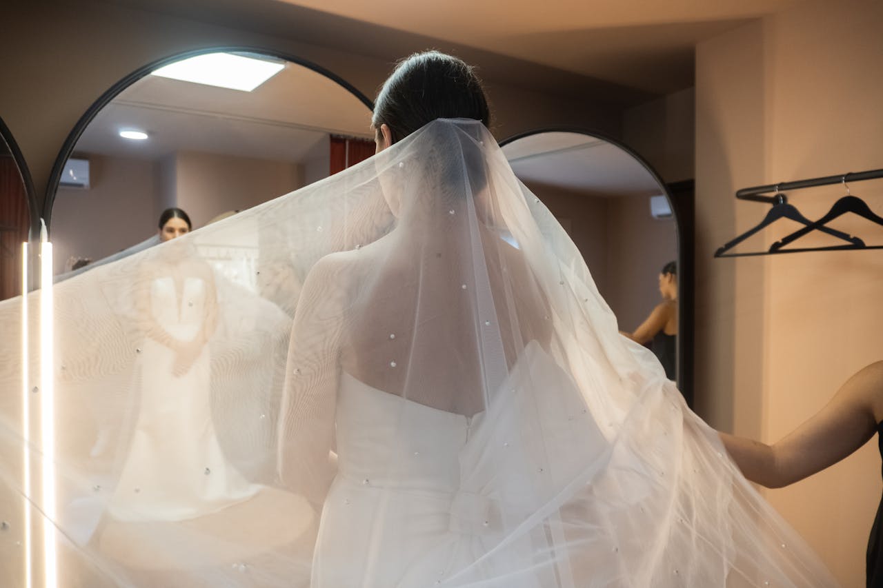 A bride in an elegant wedding dress with a long veil, captured in a mirror reflection.