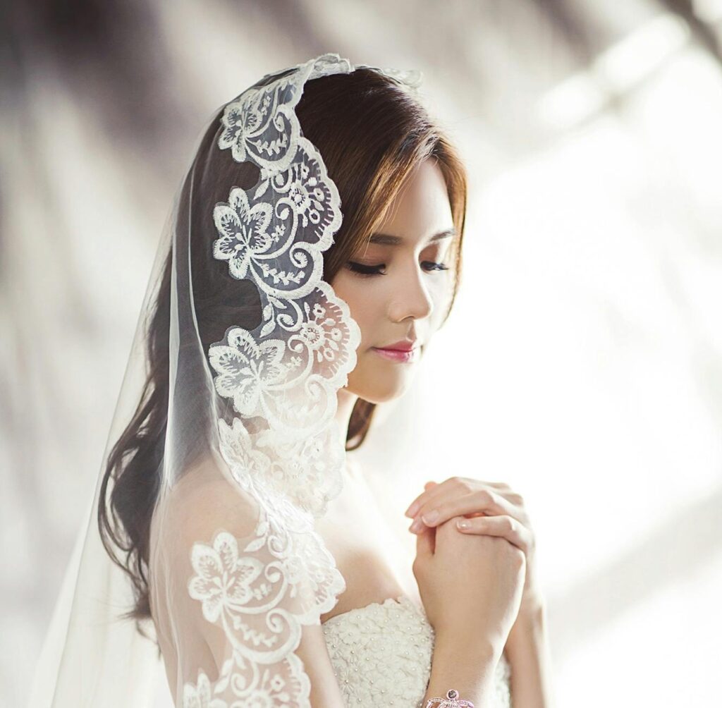 Beautiful bride in lace gown and veil, captured in soft lighting.